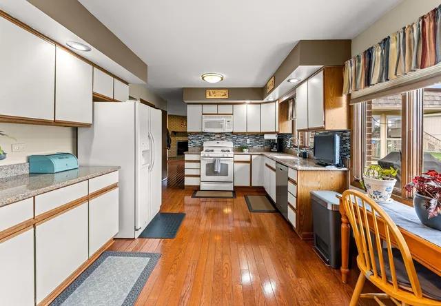 a kitchen with stainless steel appliances a stove a sink a refrigerator and white cabinets with wooden floor