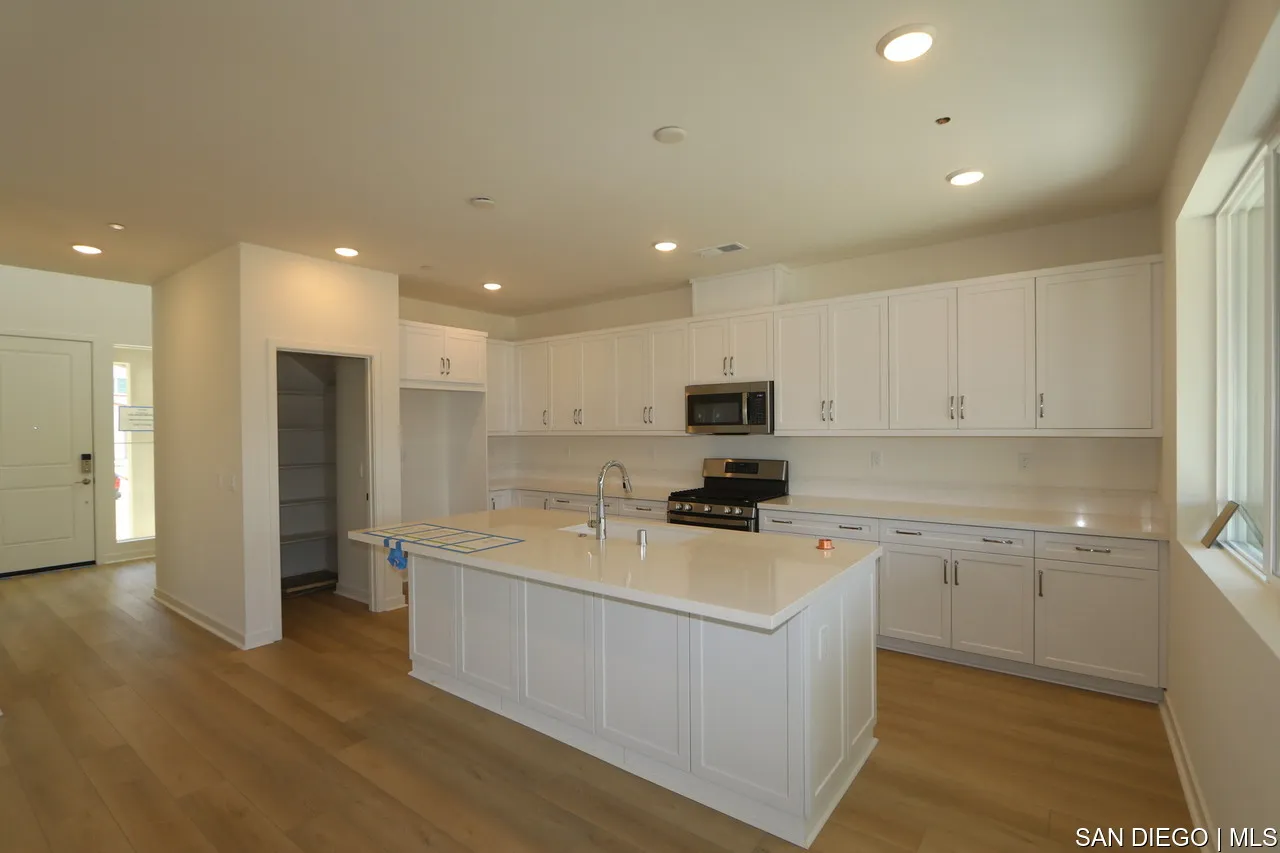 592 Meadowood Street, Unit 405 Fallbrook, CA 92028 - Photo 2 of 9 a kitchen with stainless steel appliances a stove top oven a refrigerator a sink and white cabinets with wooden floor