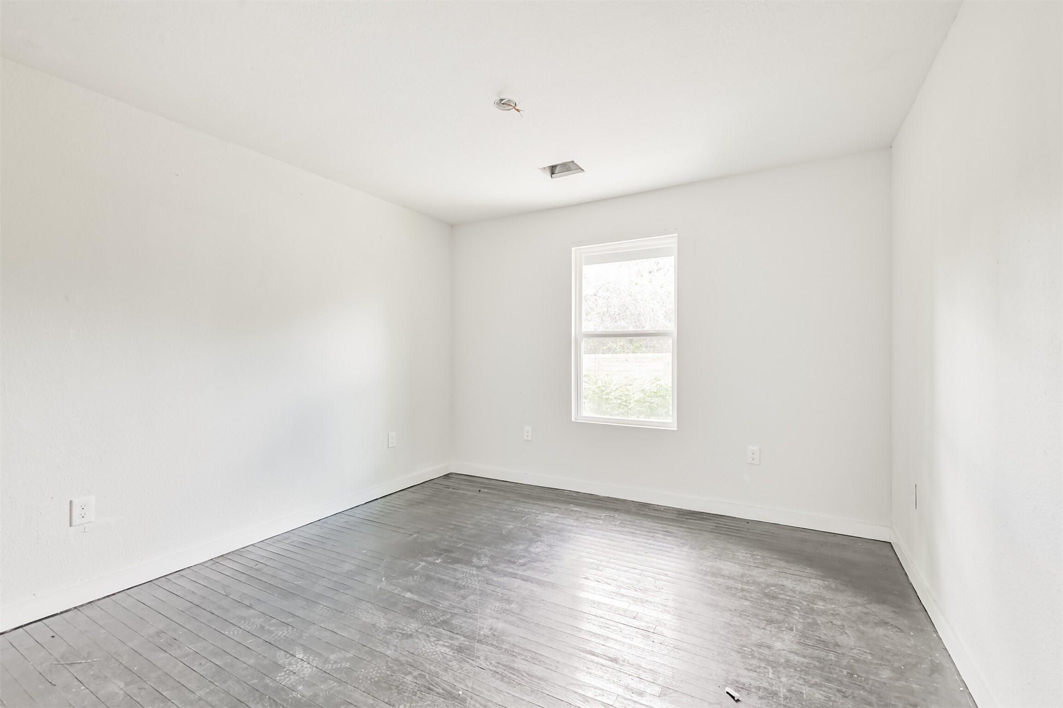 209 Leago Street Houston, TX 77022 - Photo 14 of 24 This photo shows a bright, empty room with white walls and a single window, featuring dark hardwood floors. It's a blank canvas ready for customization.