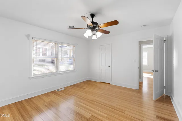 an empty room with wooden floor fan and windows