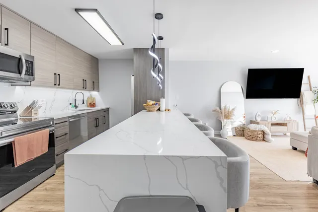 a living room with stainless steel appliances kitchen island granite countertop a sink a stove and a wooden floors