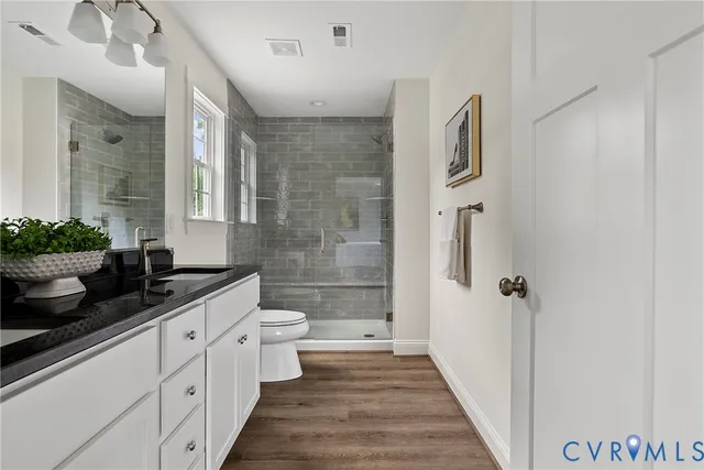 a spacious bathroom with a granite countertop sink a toilet a mirror and shower