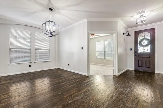 an empty room with wooden floor chandelier and windows