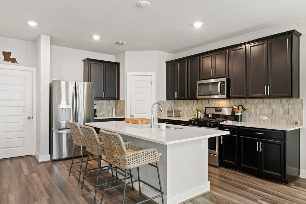 7403 Travertine Spring Drive, Unit 117 Austin, TX 78744 - Photo 2 of 37 A contemporary kitchen features dark cabinetry, stainless steel appliances, and a central island with bar seating.
