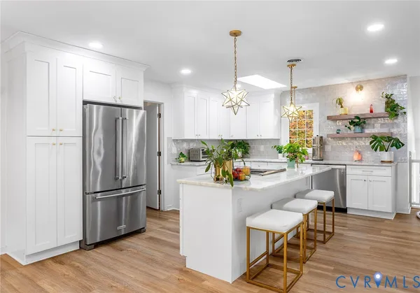 a kitchen with stainless steel appliances a refrigerator a sink cabinets a wooden floor and a chandelier