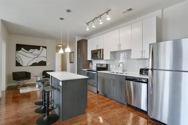 a kitchen with stainless steel appliances a refrigerator a stove a sink dishwasher and a dining table with wooden floor