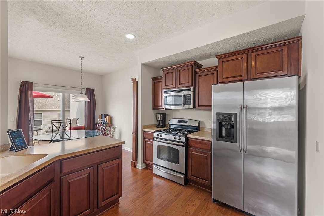 3967 Gardiner Run Akron, OH 44321 - Photo 13 of 35 Kitchen with stainless steel appliances, decorative light fixtures, a textured ceiling, light countertops, dark brown cabinets, and light hardwood flooring