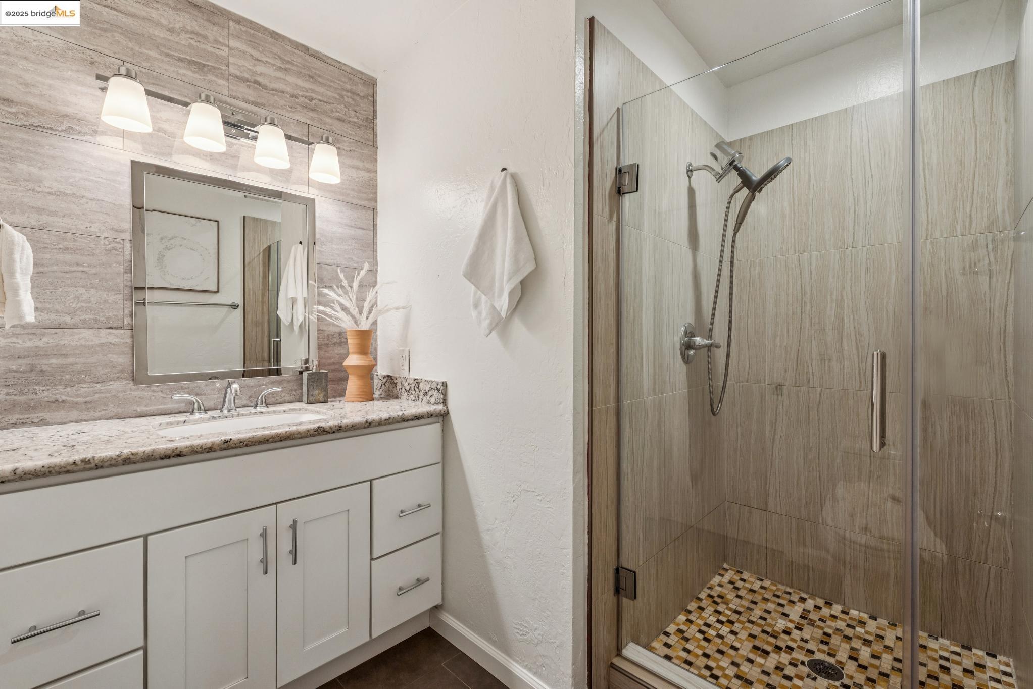 651 Oakland Avenue, Unit 1E Oakland, CA 94611 - Photo 17 of 28 a bathroom with a granite countertop sink a mirror and shower