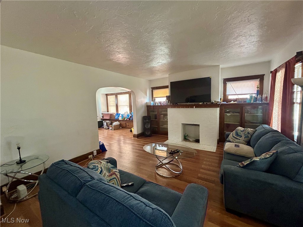 10202 Kinsman Road Cleveland, OH 44104 - Photo 2 of 15 Living area with wood finished floors, arched walkways, a textured ceiling, and a fireplace with flush hearth