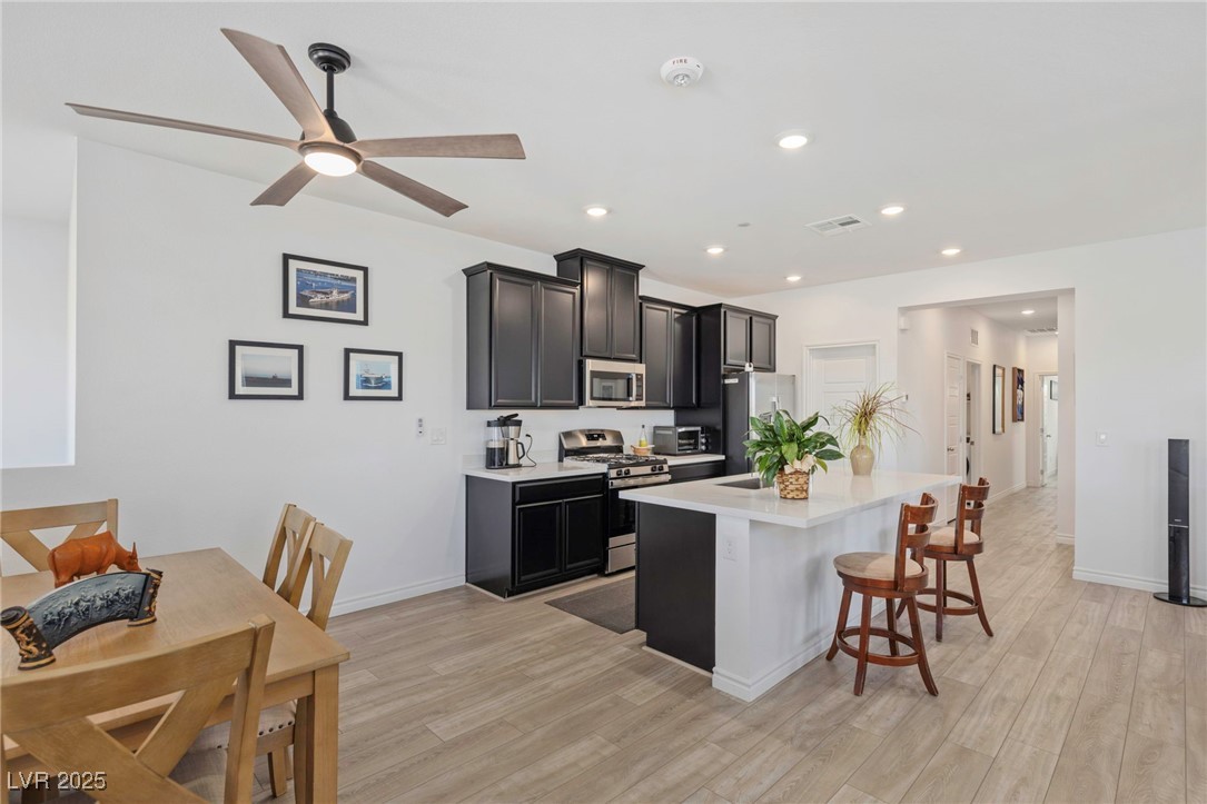 7230 North Decatur Boulevard, Unit 6 North Las Vegas, NV 89084 - Photo 3 of 27 Kitchen featuring appliances with stainless steel finishes, light countertops, a breakfast bar, a center island with sink, and light wood-style floors