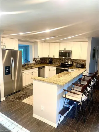 a kitchen with stainless steel appliances granite countertop a refrigerator a stove a sink a dining table and chairs with wooden floor