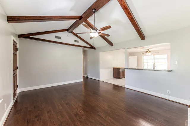 a view of an empty room with wooden floor and a ceiling fan