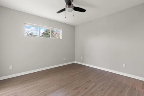 a view of an empty room with wooden floor and a ceiling fan