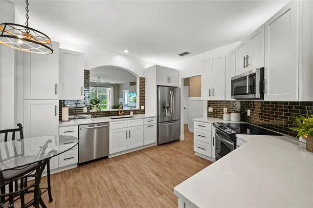 a kitchen with stainless steel appliances a microwave a stove a sink dishwasher a refrigerator and white cabinets with wooden floor