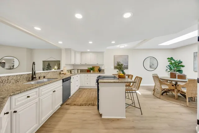 a open kitchen with granite countertop a sink and white cabinets with wooden floor