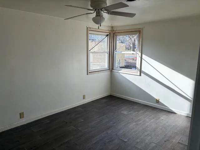 an empty room with wooden floor fan and windows