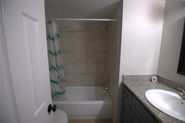 a bathroom with a granite countertop bathtub shower sink vanity and toilet
