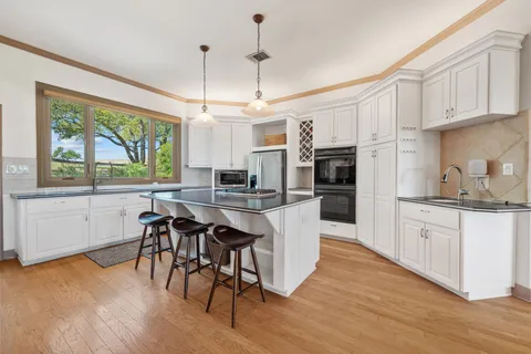 a kitchen with stainless steel appliances granite countertop a kitchen island hardwood floor sink stove dining table and chairs