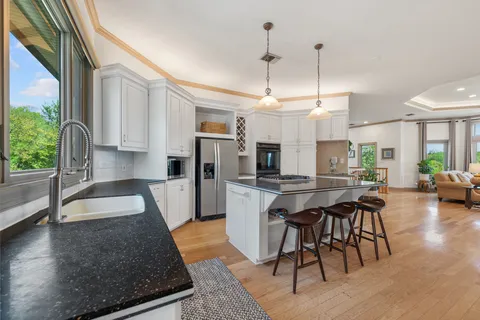 a kitchen with stainless steel appliances granite countertop a stove top oven a sink a dining table and chairs with wooden floor
