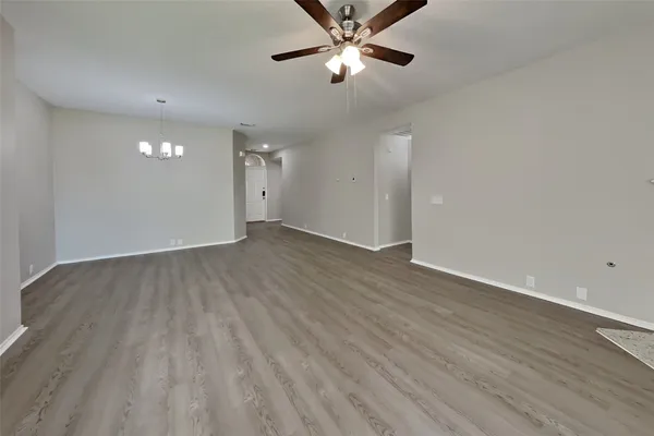 a view of an empty room with wooden floor and a ceiling fan