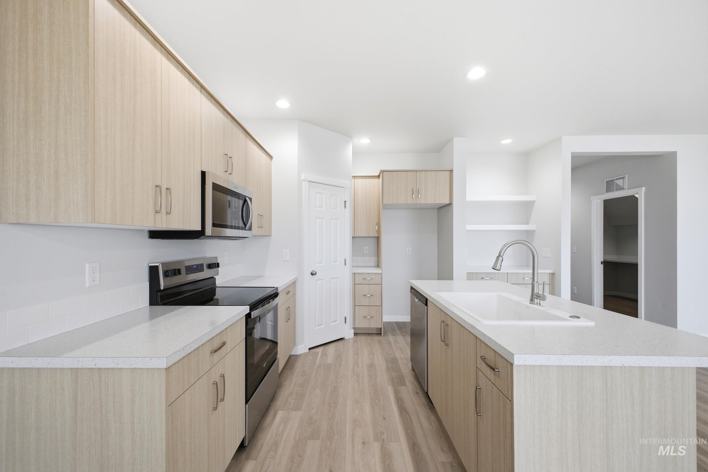 14104 Shiny Spruce Street Caldwell, ID 83607 - Photo 5 of 20 Modern kitchen featuring light wood-finish cabinetry, light-toned countertops, stainless steel appliances, and a central island with an integrated sink