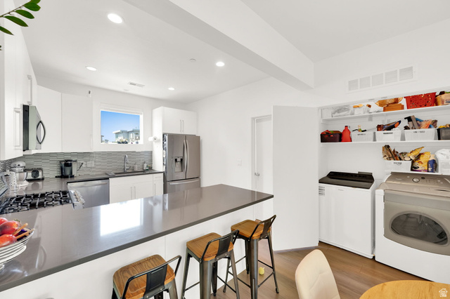 7713 Navarro View Court Midvale, UT 84047 - Photo 12 of 41 Modern kitchen featuring white cabinetry, stainless steel appliances, a grey countertop island, and wood-finish flooring