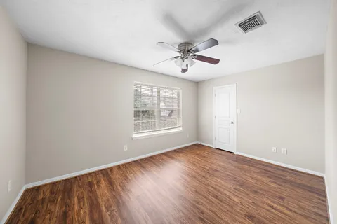 a view of empty room with wooden floor and fan