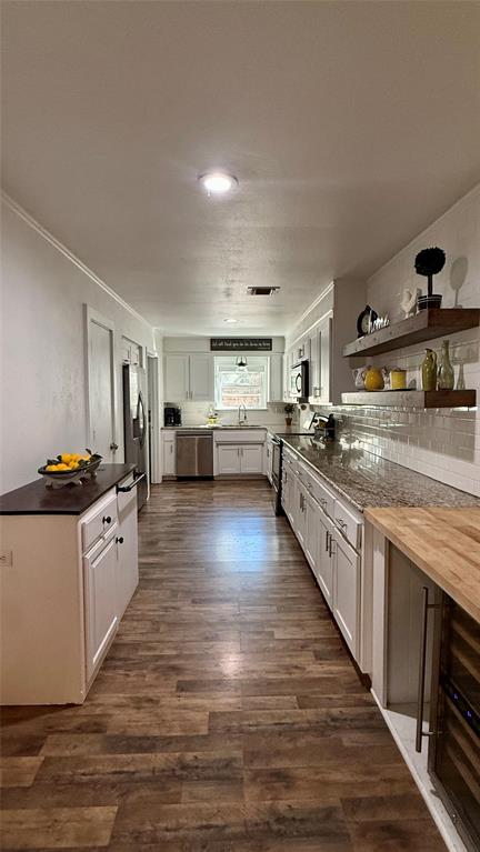 8513 Ravenswood Road Granbury, TX 76049 - Photo 10 of 21 Galley kitchen featuring wood-finish flooring, white cabinetry, granite-style countertops, stainless steel appliances, and a tile backsplash