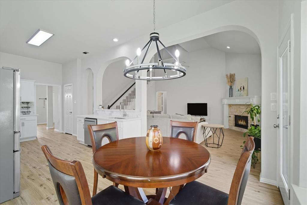 409 Springtree Road Lake Dallas, TX 75065 - Photo 22 of 40 Open-concept living area featuring light wood-finish flooring, a contemporary chandelier, arched entryways, and a stone-faced fireplace with a mantel