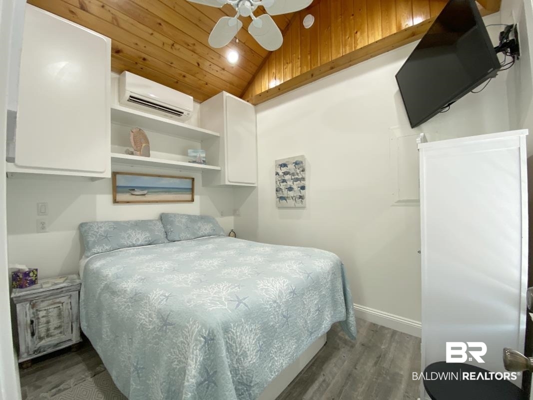 28888 Canal Road, Unit 77 Orange Beach, AL 36561 - Photo 12 of 23 Interior bedroom featuring wood-finish flooring, a pitched wood-paneled ceiling, integrated wall shelving, a mounted television, and a mini-split air conditioning unit