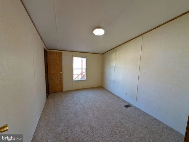 a view of an empty room with window and kitchen view