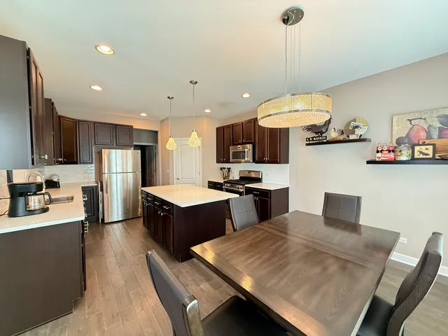 a kitchen with stainless steel appliances granite countertop a sink dishwasher a refrigerator a stove a kitchen island and chairs with wooden floor