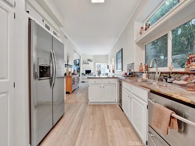 a kitchen with stainless steel appliances granite countertop a refrigerator a sink dishwasher a stove and white countertops with wooden floor