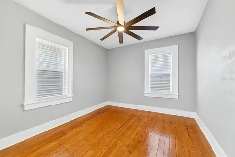 an empty room with wooden floor windows and fan