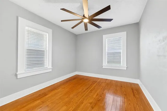 an empty room with wooden floor windows and fan