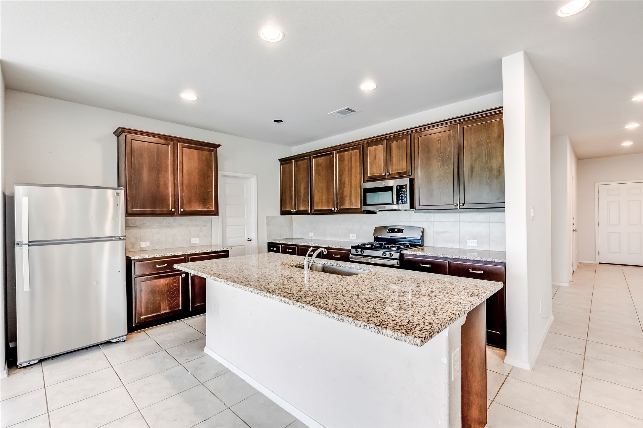 2721 Winding Creek Road Kyle, TX 78640 - Photo 10 of 27 Kitchen featuring a central island with a granite countertop, dark wood-finish cabinetry, stainless steel appliances, and recessed lighting