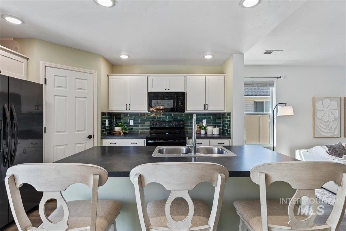 12781 Ashfield Street Caldwell, ID 83607 - Photo 12 of 30 Kitchen featuring dark countertops, black appliances, a kitchen breakfast bar, and white cabinetry