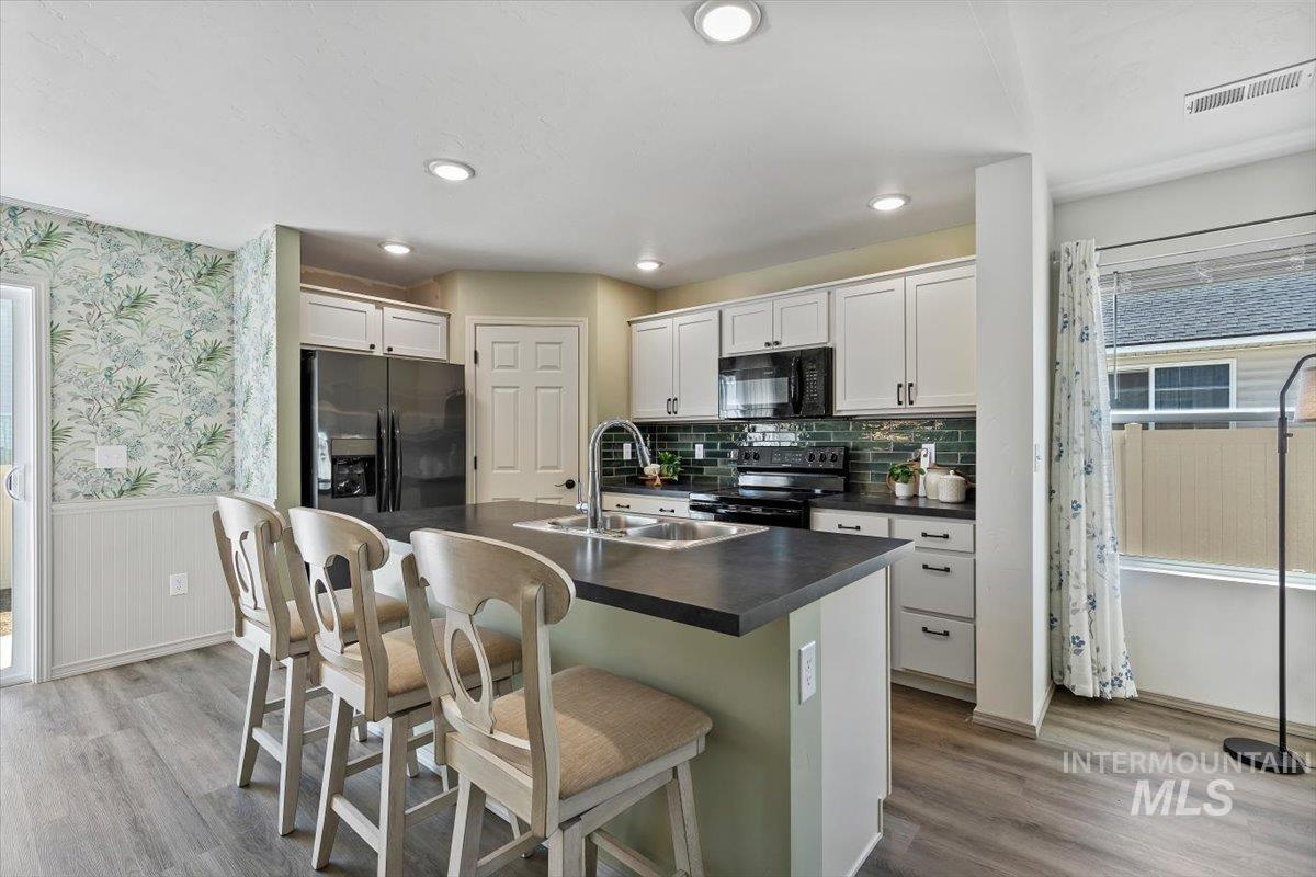 12781 Ashfield Street Caldwell, ID 83607 - Photo 9 of 30 Kitchen with a breakfast bar, dark countertops, a center island with sink, black appliances, and white cabinetry