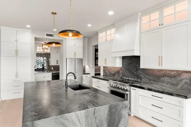 a kitchen with stainless steel appliances granite countertop a stove a sink a refrigerator and white cabinets