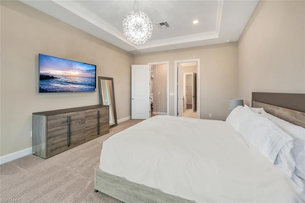 8448 Rosa Court Naples, FL 34114 - Photo 15 of 24 Spacious bedroom featuring neutral wall tones, tray ceiling with recessed lighting, and a modern chandelier