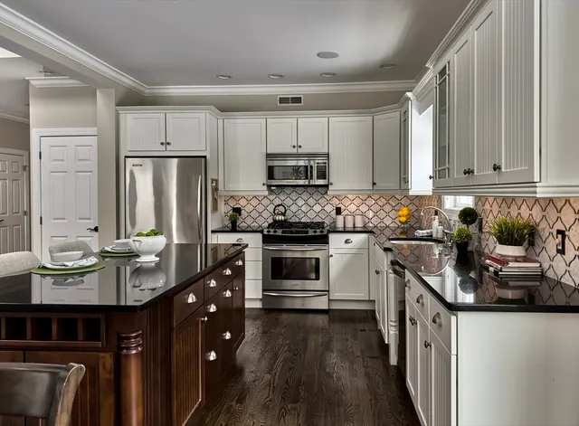 a kitchen with stainless steel appliances granite countertop a stove top oven a sink dishwasher a dining table and chairs with wooden floor