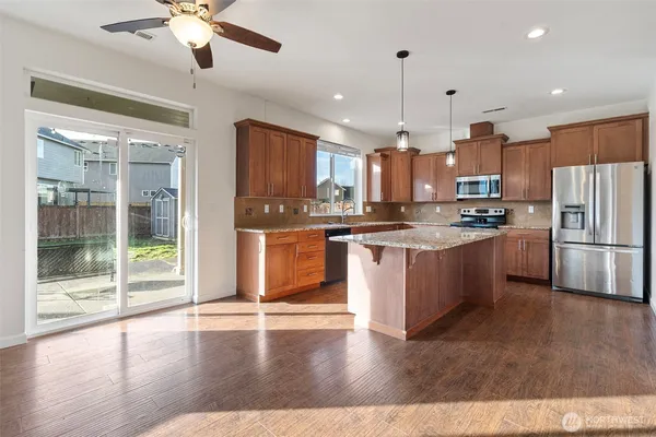 a open kitchen with stainless steel appliances granite countertop a stove top oven a refrigerator a sink and a dining table with wooden floor