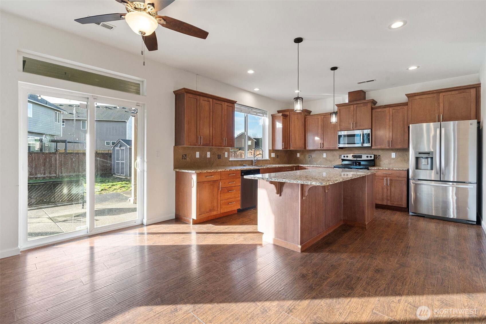 204 Balmer Street Southwest Orting, WA 98360 - Photo 6 of 29 a open kitchen with stainless steel appliances granite countertop a stove top oven a refrigerator a sink and a dining table with wooden floor