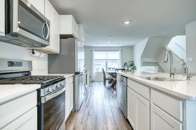 a kitchen with stainless steel appliances granite countertop a stove top oven a sink dishwasher a dining table and chairs with wooden floor