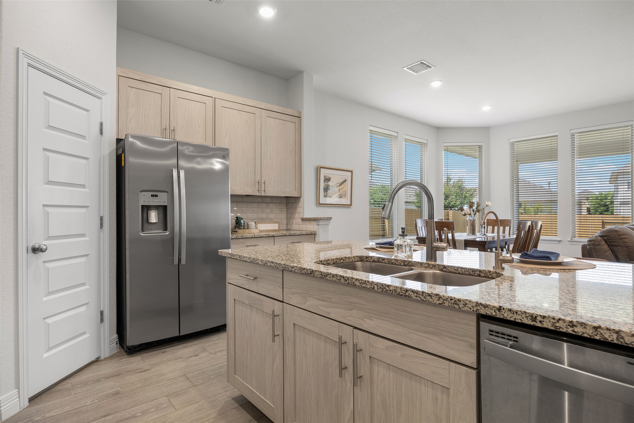 704 Muster Bend Georgetown, TX 78626 - Photo 10 of 38 Kitchen with light wood finish cabinets, stainless steel appliances, light wood finished floors, light stone countertops, and decorative backsplash