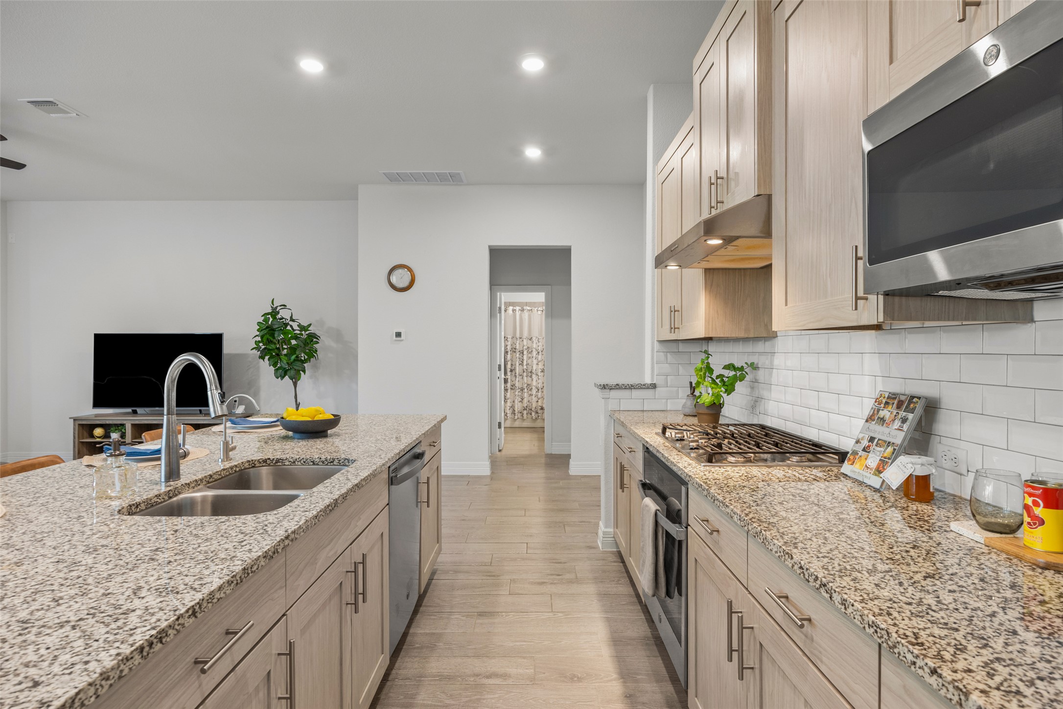 704 Muster Bend Georgetown, TX 78626 - Photo 10 of 39 Kitchen featuring stainless steel appliances, light stone countertops, recessed lighting, decorative backsplash, and light wood finished floors