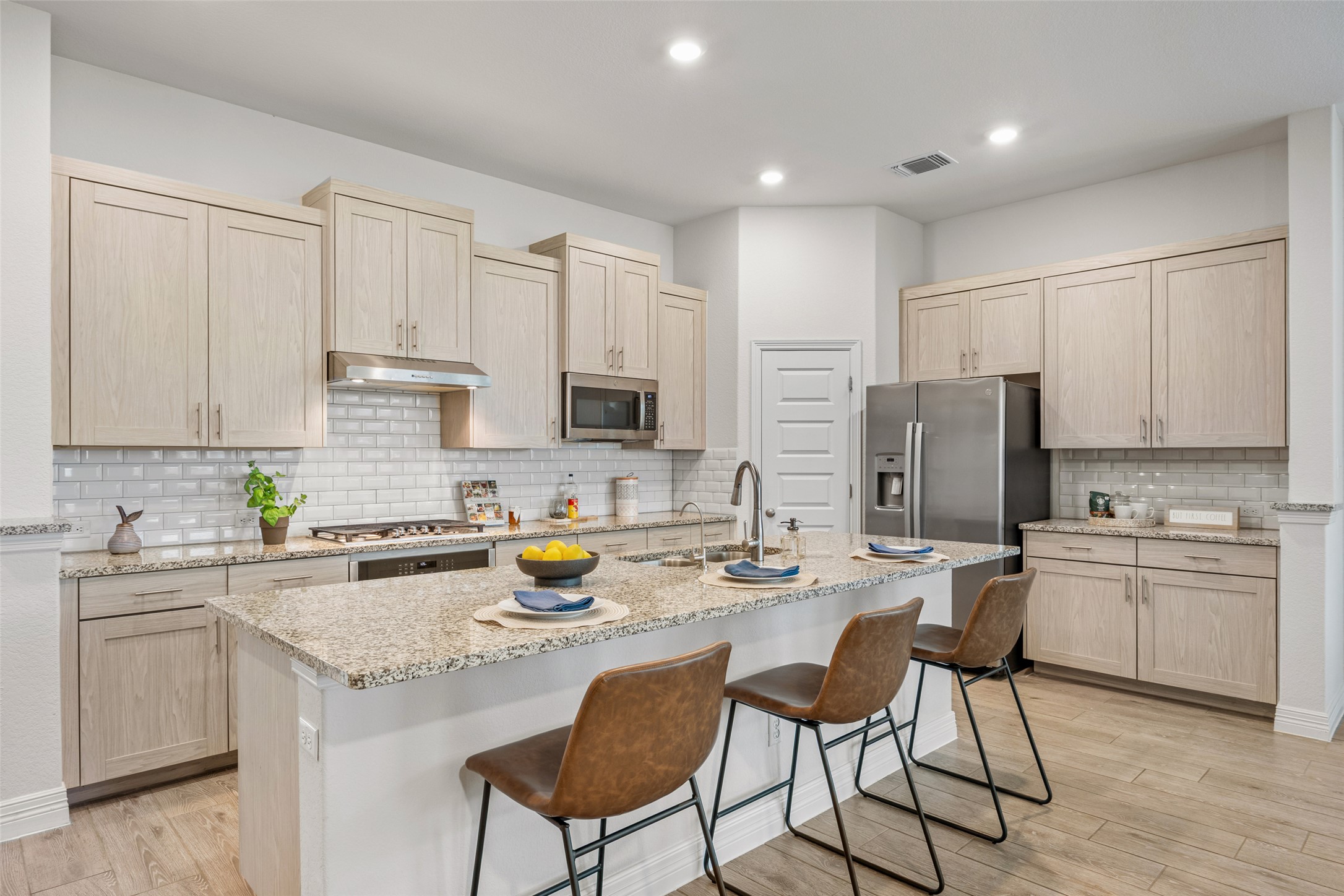 704 Muster Bend Georgetown, TX 78626 - Photo 6 of 38 Kitchen with light stone counters, light wood-type flooring, a kitchen bar, a kitchen island with sink, and light wood finish cabinetry