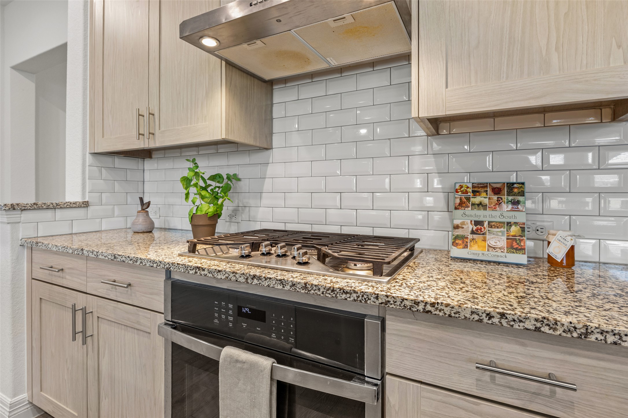 704 Muster Bend Georgetown, TX 78626 - Photo 9 of 39 Kitchen featuring range hood, stainless steel appliances, light wood finish cabinetry, light stone counters, and decorative backsplash