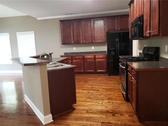 a kitchen with stainless steel appliances granite countertop a stove top oven a refrigerator a sink and dishwasher with wooden floor