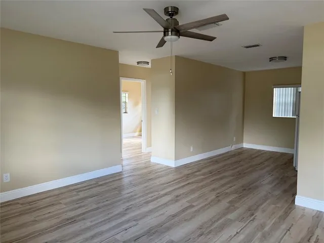 a view of an empty room with wooden floor and a ceiling fan